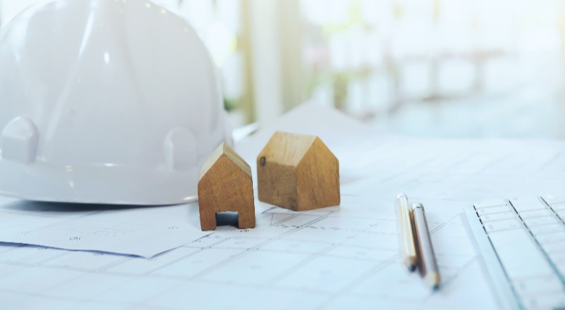 White hard hat on table alongside property development blueprints and plans.